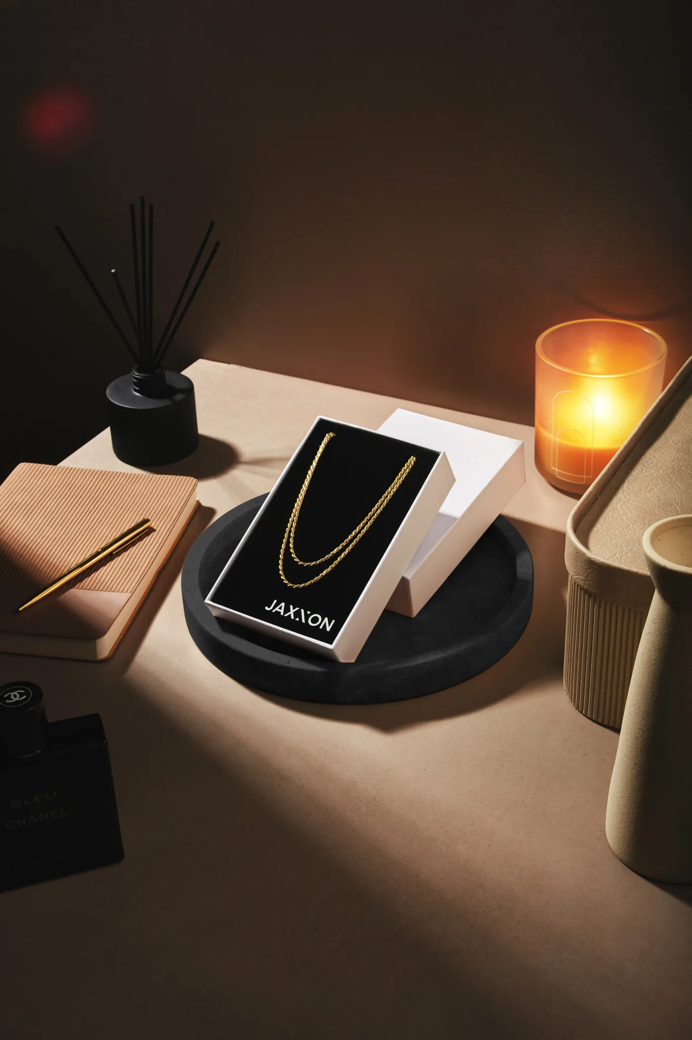 The chain in its open JAXXON box on a tray, by a candle